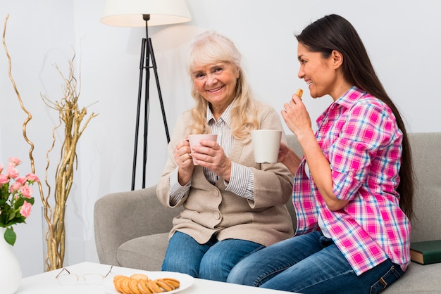 Feliz retrato de una madre y una hija sentada en el sofá desayunando juntas