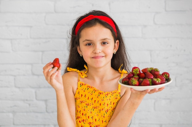 Feliz retrato de una niña con fresa y plato en sus manos