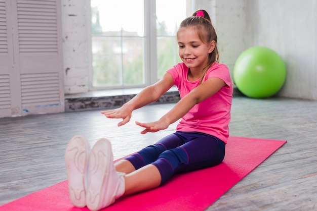 Feliz retrato de una niña sentada en una estera de ejercicios estirando sus manos