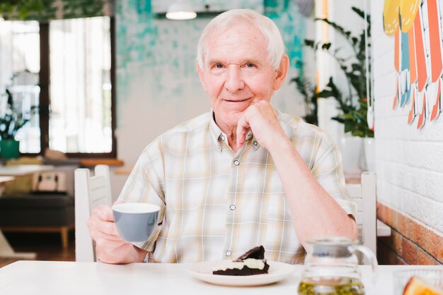 Feliz senior masculino sentado en la cafetería disfrutando de té y postre