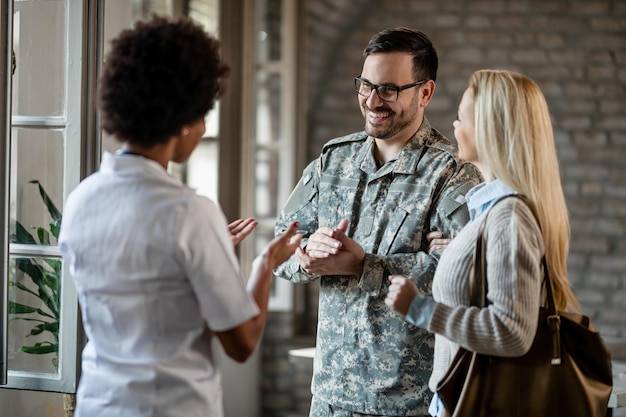 Feliz soldado del ejército y su esposa comunicándose con un trabajador de la salud afroamericano mientras consultan en la clínica