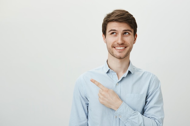 Feliz sonriente guapo mirando y apuntando hacia la esquina superior izquierda de la bandera