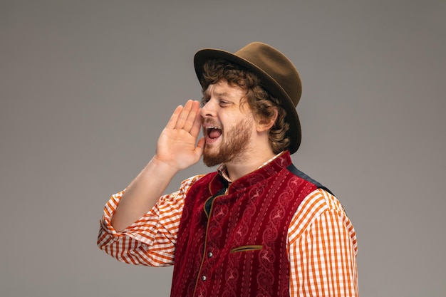 Feliz sonriente hombre vestido con traje tradicional austriaco o bávaro gesticulando aislado en gris