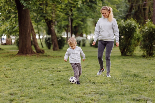 Feliz sonriente madre e hijos jugando con pelota de fútbol al aire libre