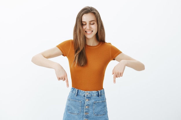 Feliz sonriente mujer atractiva mirando satisfecho y apuntando hacia abajo