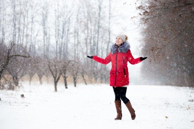 Feliz sonriente mujer en chaqueta de invierno rojo disfruta de la nieve, al aire libre, en el parque