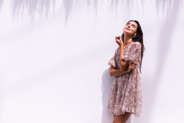 Feliz sonriente mujer de pelo largo en vestido se encuentra en la pared blanca