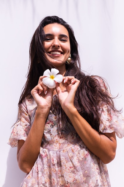 Feliz sonriente mujer de pelo largo en vestido se encuentra en la pared blanca