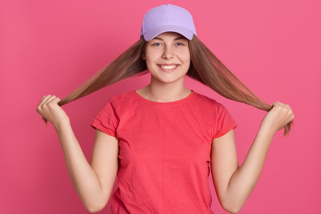 Foto gratuita feliz sonriente mujer vestida con camiseta roja y gorra de béisbol empujando su cabello a un lado