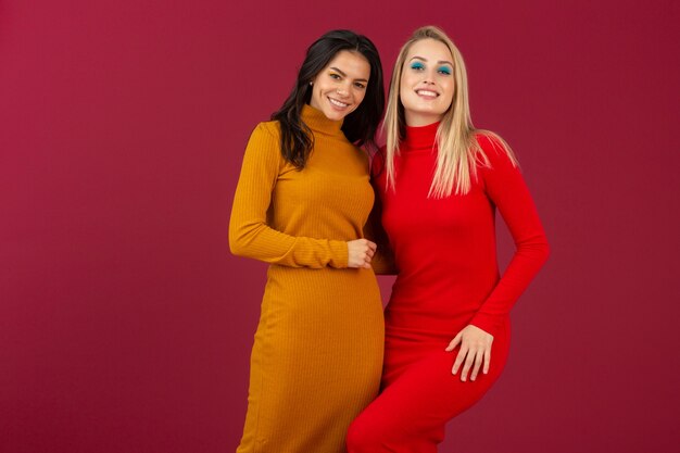 Feliz sonriente a mujeres muy elegantes en amarillo y rojo otoño invierno vestido de punto de moda posando aislado en la pared roja