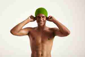 Foto gratuita feliz sonriente nadador afroamericano poniéndose su gorro de baño verde mirando en blanco