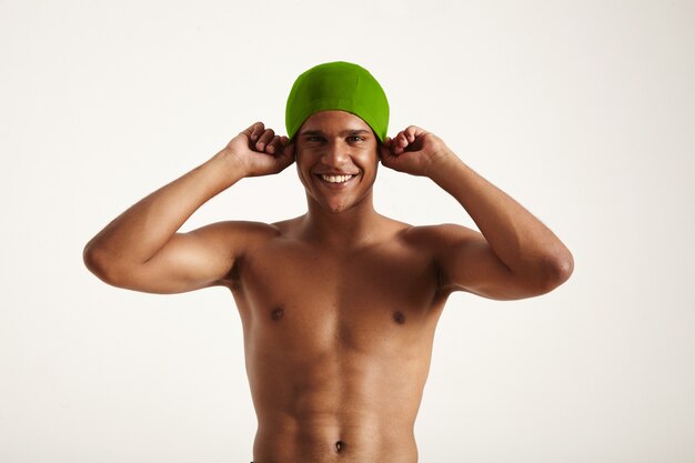 Feliz sonriente nadador afroamericano poniéndose su gorro de baño verde mirando en blanco