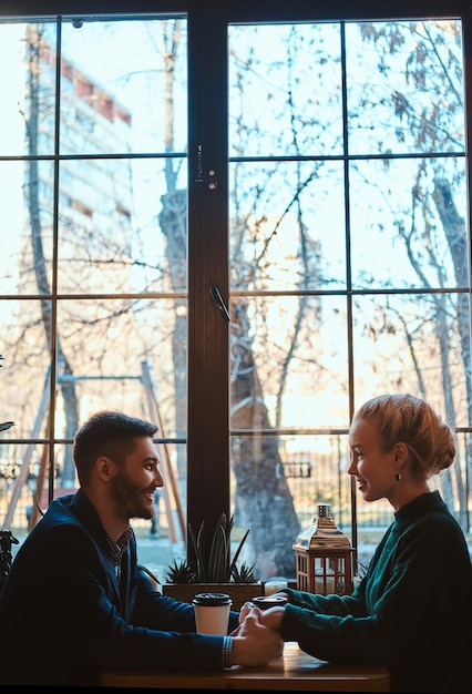 Feliz sonriente pareja de gente atractiva sentada y tomando café y calentándose con café.