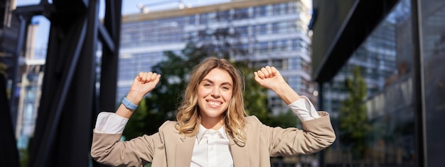 Foto gratuita una feliz y sonriente vendedora con traje beige celebra su logro triunfando haciendo puñetazos y