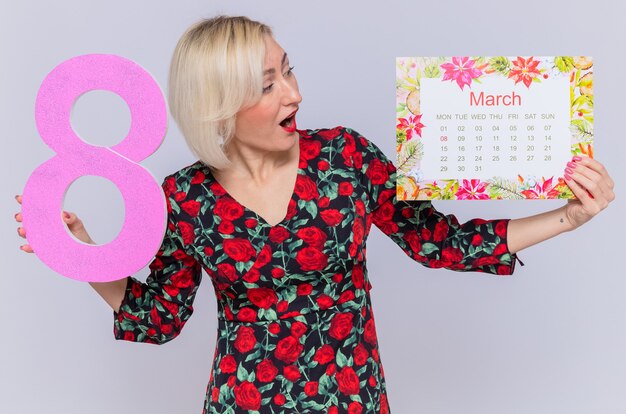 Feliz y sorprendida joven sosteniendo un calendario de papel del mes de marzo y el número ocho, celebrando el día internacional de la mujer
