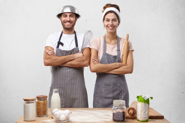 Feliz y talentosa familia europea joven cocineros masculinos y femeninos vistiendo delantales y sosteniendo instrumentos,