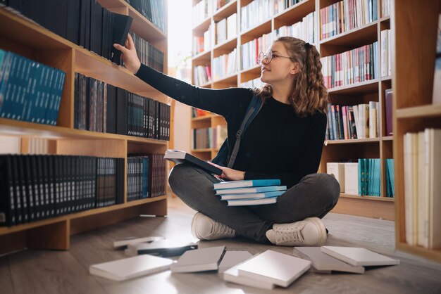 Feliz tenage girl o estudiante tomando un libro del estante en la biblioteca - Concepto de gente, conocimiento, educación y escuela