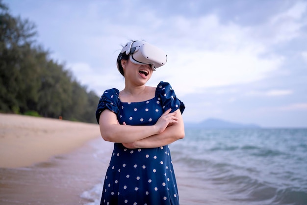 Feliz, alegre, atractiva, mujer adulta asiática, casual con gafas de tecnología vr de en la playa y ajustando el dispositivo para ver video digital virtual de simulación 3d en