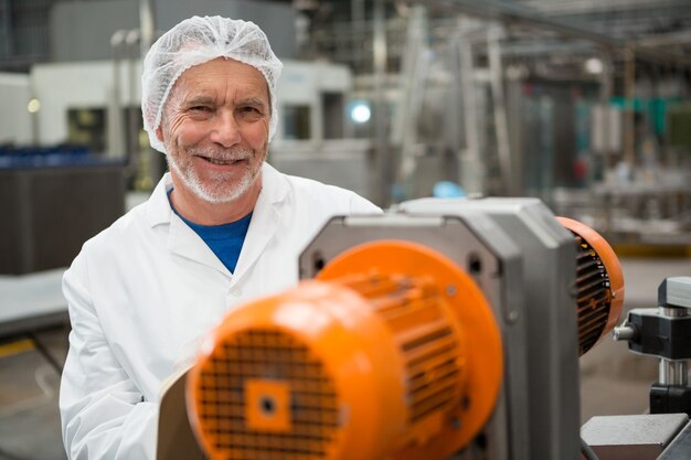 Feliz trabajador masculino de pie junto a las máquinas en la fábrica de bebidas frías