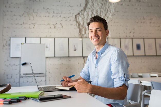 Feliz trabajador remoto joven guapo pensando, escribiendo notas en el cuaderno