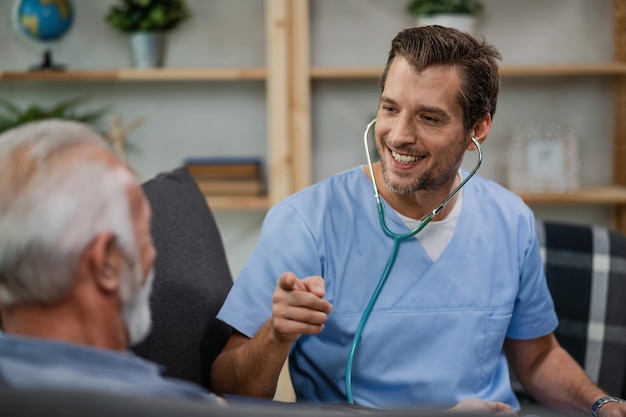 Foto gratuita feliz trabajador de la salud comunicándose con un anciano y señalándolo mientras estaba en una visita a casa