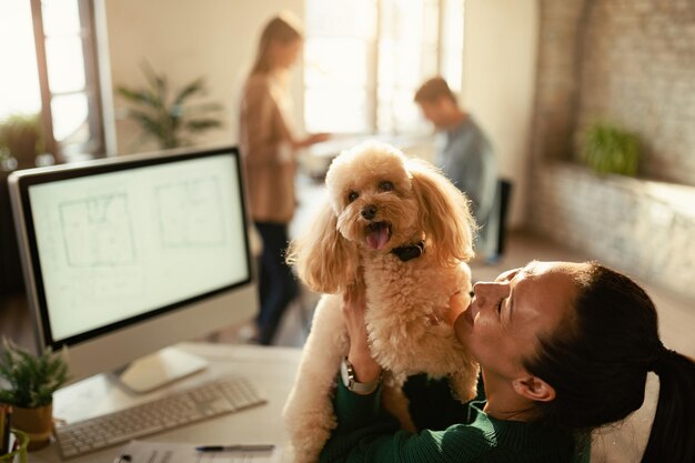 Feliz trabajadora independiente asiática divirtiéndose con su caniche en la oficina