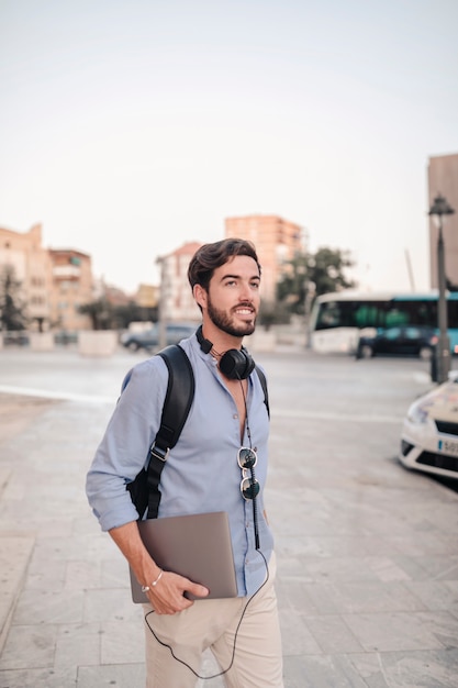 Foto gratuita feliz turista masculino con portátil caminando sobre el pavimento