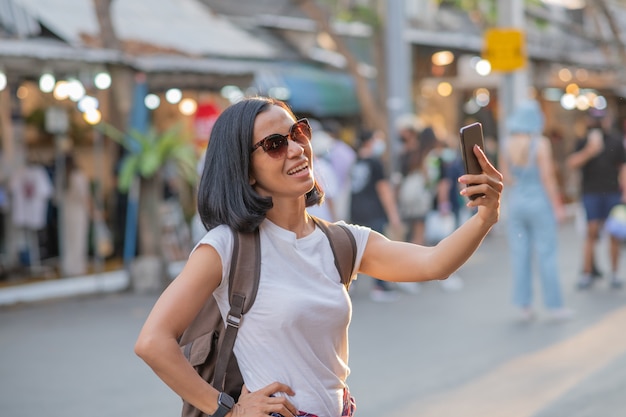 Feliz viaje joven mujer asiática con teléfono móvil y relajarse en la calle.