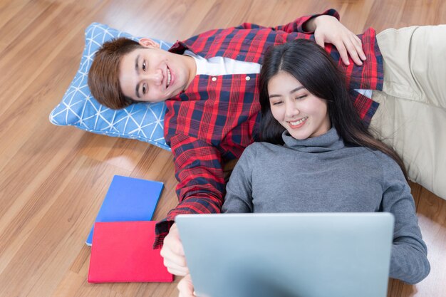 Felizmente joven y bella mujer acostada en el piso de madera y usando laptop