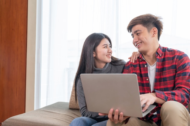 Felizmente joven y bella mujer y hombre guapo usando la computadora portátil en el sofá en el dormitorio en casa