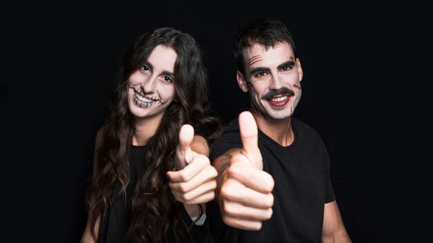 Femenino y masculino con maquillaje espeluznante, poniendo los pulgares arriba