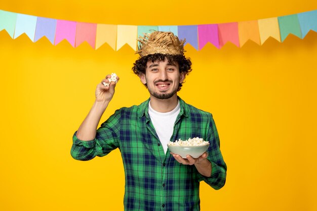 Festa junina chico lindo joven con sombrero de paja y banderas coloridas festival brasileño lanzando palomitas de maíz