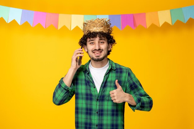 Festa junina chico lindo joven en sombrero de paja y banderas coloridas festival brasileño en la llamada telefónica