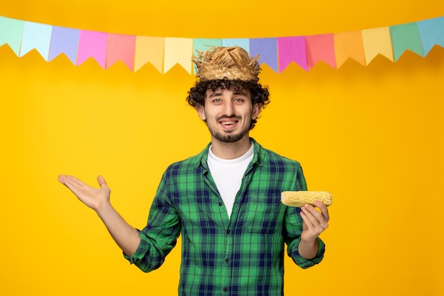Festa junina chico lindo joven con sombrero de paja y banderas coloridas festival brasileño sosteniendo maíz sonriendo