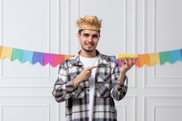 Festa junina guapo chico encantador en camisa con sombrero de paja celebrando el festival con maíz