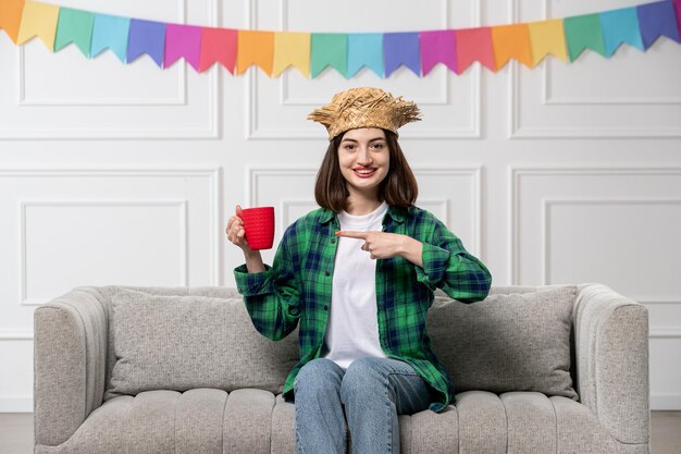 Festa junina linda chica encantadora en camisa verde sombrero de paja con banderas de colores con taza roja