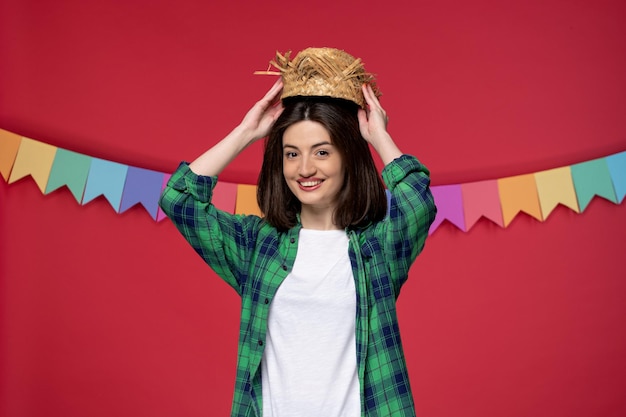 Foto gratuita festa junina linda joven con camisa verde celebrando el festival brasileño quitándose el sombrero de paja