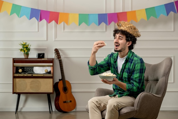 Festa junina lindo joven con sombrero de paja con radio retro y banderas coloridas comiendo palomitas de maíz