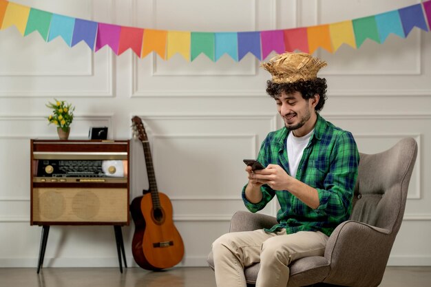 Festa junina lindo joven con sombrero de paja con radio retro y banderas coloridas escribiendo en el teléfono