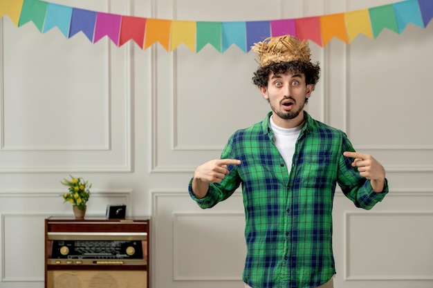 Festa junina lindo joven con sombrero de paja con radio retro y banderas coloridas sorprendido