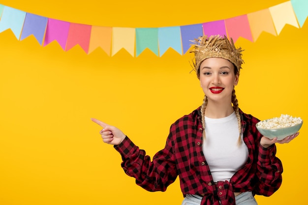 Festa junina rubia linda chica en sombrero de paja festival brasileño con banderas coloridas señalando con el dedo