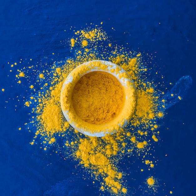 Festival de holi indio de color amarillo en un tazón sobre fondo azul