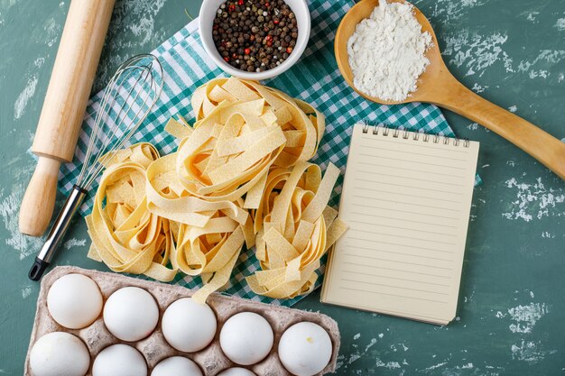 Fettuccine con huevos, rodillo, batidor, granos de pimienta, almidón y cuaderno