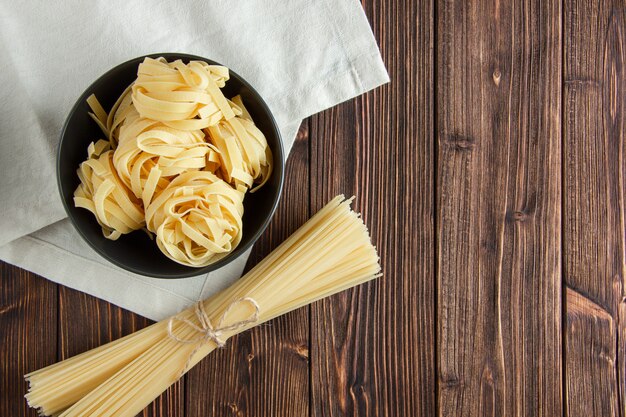 Fettuccine pasta con espagueti en un recipiente sobre fondo de madera y papel de cocina, plano.