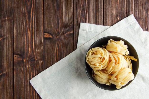 Fettuccine pasta en un recipiente sobre fondo de madera y toalla de cocina. aplanada