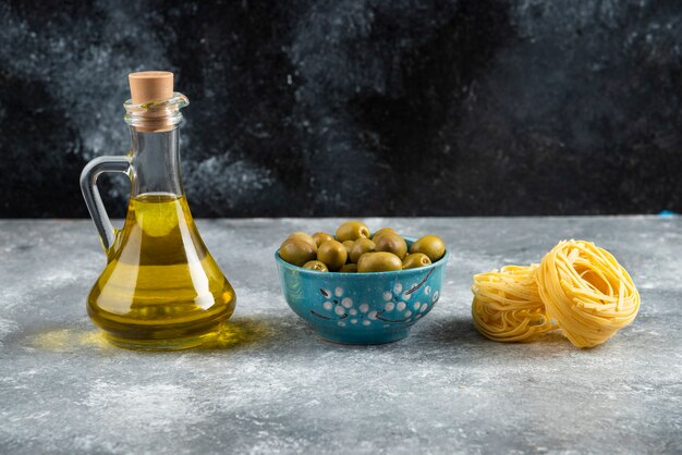 Fideos, aceite y aceitunas verdes sobre mesa de piedra.