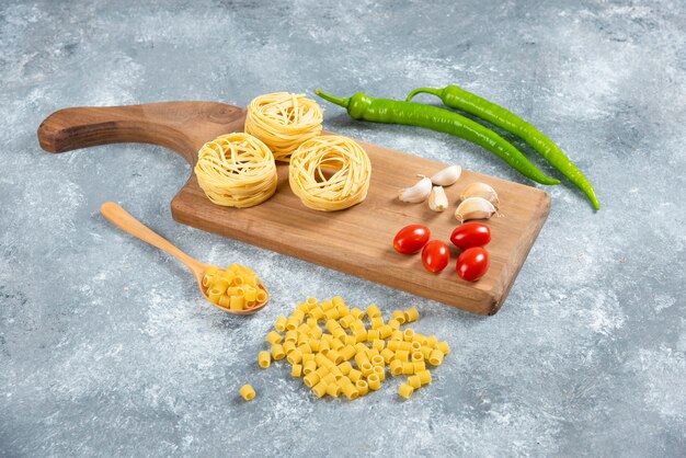 Fideos, ajo y tomates sobre tabla de madera.