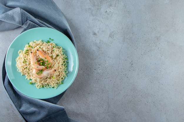 Fideos y camarones en un plato sobre un trozo de tela, sobre el fondo de mármol.