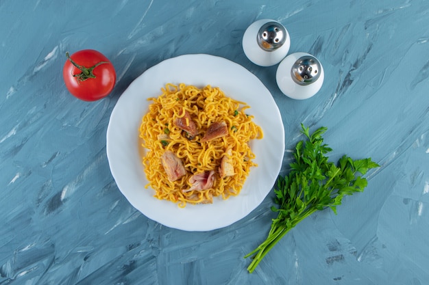 Foto gratuita fideos con carne en un plato junto al manojo de perejil, tomates y sal, sobre el fondo de mármol.