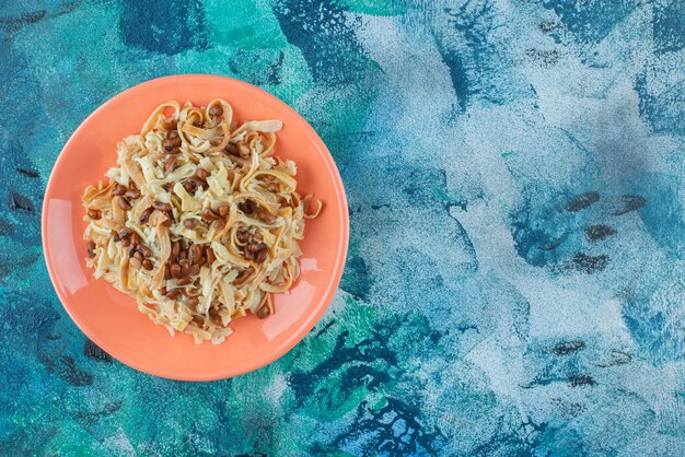 Fideos caseros con frijoles en un plato sobre salvamanteles, sobre fondo azul.